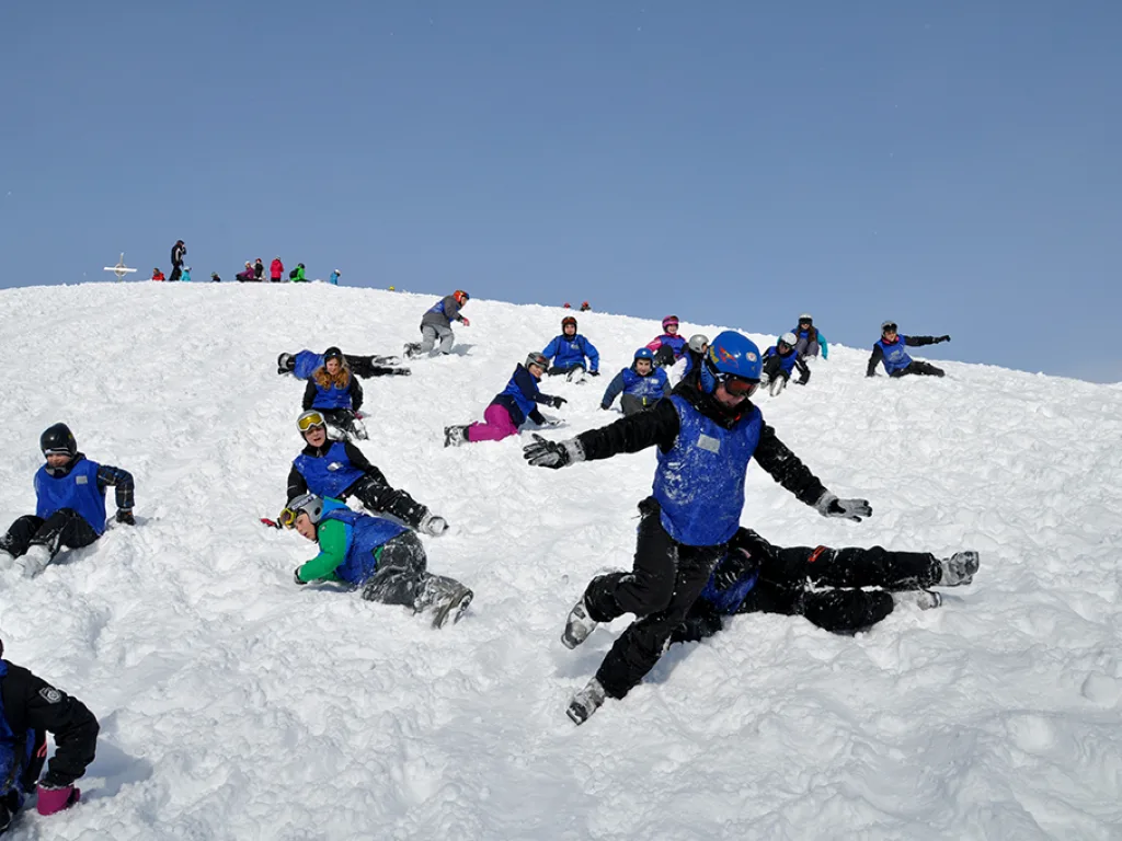 Jugendliche rutschen und liegen auf einer Schneekuppe.